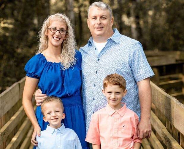 A full shot of Malissa Black on a wooden bridge with her husband and two children.